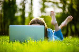 Young woman laying down relaxed in park is working or studying on laptop